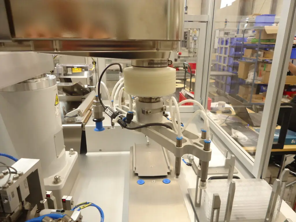 Für die **automatisierte Verpackung medizinischer Komponenten** haben wir eine **kundenspezifische Verpackungsmaschine für Sonderverpackungen** realisiert, die auf sensible Produkte und hohe Anforderungen an **Sauberkeit, Prozesssicherheit und reproduzierbare Verpackungsqualität** ausgelegt ist. Die Anlage vereint **Vereinzelung, positionssicheres Handling, Verpacken, Vakuumieren und Verschweißen** in einem integrierten Prozess. Ausgelegt ist die Lösung auf **zwei Produktvarianten** und auf die **Einbindung in ein bestehendes Reinraumumfeld** bei sehr kompakter Stellfläche.  Die besondere Herausforderung lag in der **schonenden und zugleich stabilen Automatisierung des Verpackungsprozesses**. Dafür wurde die Anlage mit einem **Scara-Roboter**, einem abgestimmten **Vakuumgreifsystem**, einer **kameragestützten Lage- und Füllkontrolle** sowie einer integrierten Einheit zum **Vakuumieren und Folienschweißen** aufgebaut. Der Prozess beginnt mit der geordneten Zuführung und Vereinzelung der medizinischen Komponenten. Anschließend werden Trays automatisiert bereitgestellt, die Komponenten präzise eingelegt, die Belegung optisch geprüft und die gefüllten Trays in den Verpackungsprozess überführt. Danach werden die Beutel automatisiert bereitgestellt, geöffnet, befüllt, vakuumiert, verschweißt und dem weiteren Materialfluss übergeben.  Ein zentraler Bestandteil der Lösung ist die **prozessintegrierte Qualitäts- und Handhabungssicherheit**. Eine **21-MP-Kamera** unterstützt die positionsgenaue Handhabung und überwacht die Belegung der Trays, während ein **Ionisierungssystem** stabile Bedingungen für die Verarbeitung empfindlicher Komponenten und Verpackungsmaterialien schafft. Für das Verpacken kommt ein auf medizinische Anwendungen ausgelegtes **Vakuum- und Schweißsystem** zum Einsatz, das die Schritte **Evakuieren und Verschließen** in einem kontrollierten Ablauf zusammenführt. So entsteht ein durchgängiger Verpackungsprozess, der Qualität nicht erst nachgelagert kontrolliert, sondern direkt im Prozess absichert.  Das Ergebnis ist eine **automatisierte Sonderverpackungslösung für medizinische Komponenten**, die **Handling, Traybeladung, Vakuumverpackung und Folienschweißen** in einem kompakten System vereint. Mit einer Leistung von **12 Komponenten pro Minute** und einer **technischen Verfügbarkeit von mindestens 96 %** schafft die Anlage die Grundlage für **wirtschaftliche, saubere und belastbare Verpackungsprozesse in der Medizintechnik**. Der Betreiber profitiert von hoher Prozessstabilität, geringem manuellem Eingriff und einer reproduzierbaren Verpackungsqualität auch bei variierenden Produktanforderungen.